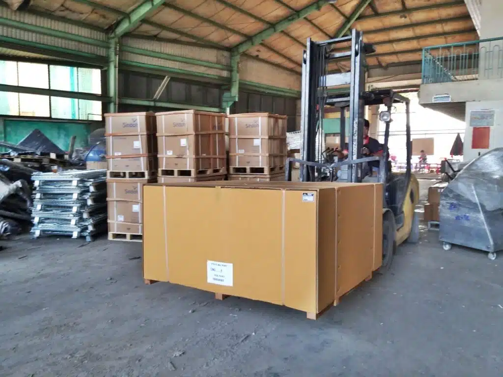 Xe nâng hạ kiện hàng đóng thùng carton lớn trong kho Vận Chuyển Á Châu, phía sau là các pallet kiện máy chờ xếp chuyến