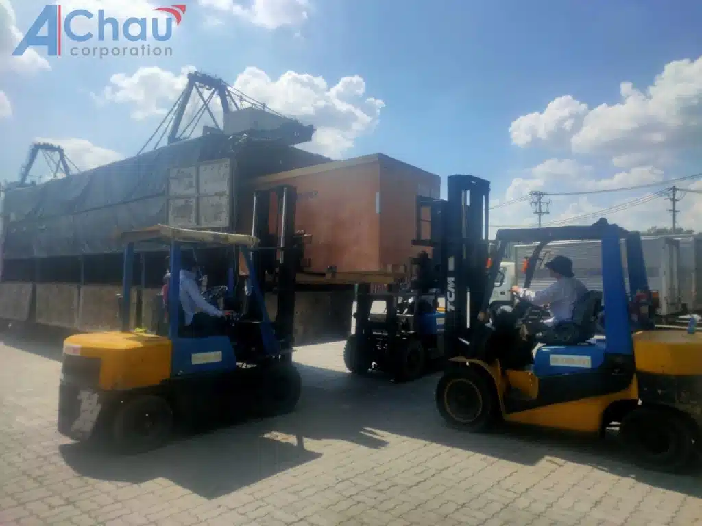 Hai xe nâng phối hợp hạ kiện máy đóng thùng gỗ từ xe thùng bạt của Á Châu xuống bãi