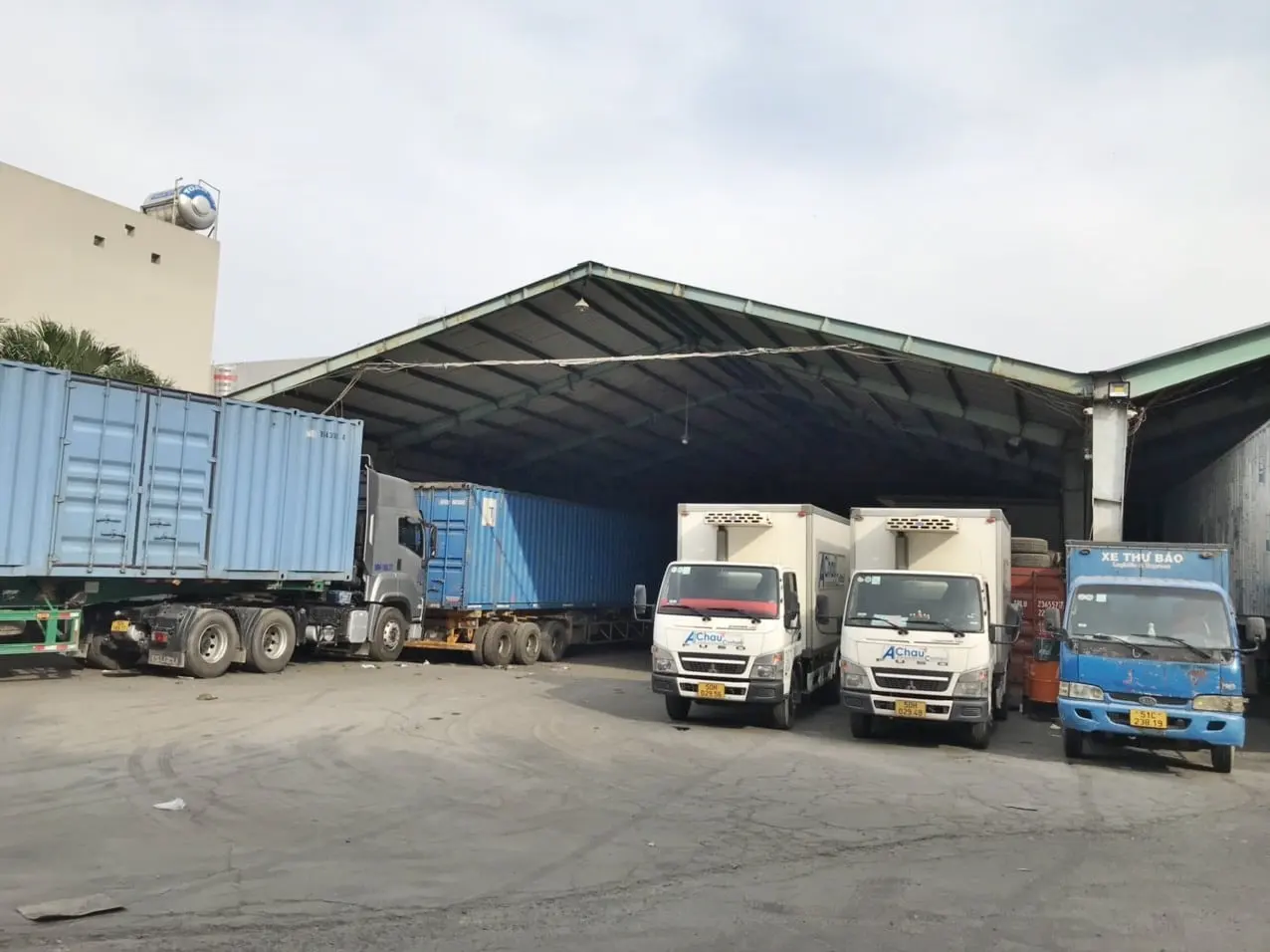 Bãi xe Á Châu với container trên mooc đậu cạnh hai xe tải nhỏ thùng kín dùng cho chặng gom và giao hai đầu