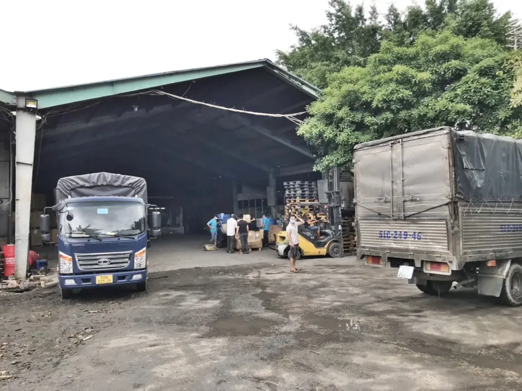 Sân kho Á Châu với xe tải và xe nâng đang bốc hàng